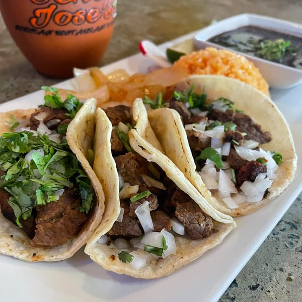 Three carne asada street tacos with cilantro and onions, served with rice and black beans.